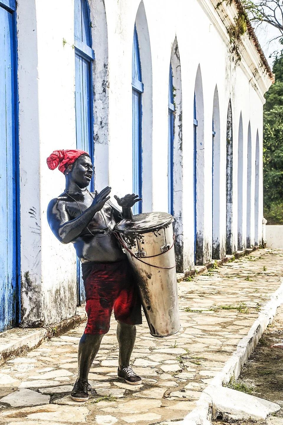 Integrante do Lambe-Sujo tocando tambor em rua de arquitetura histórica